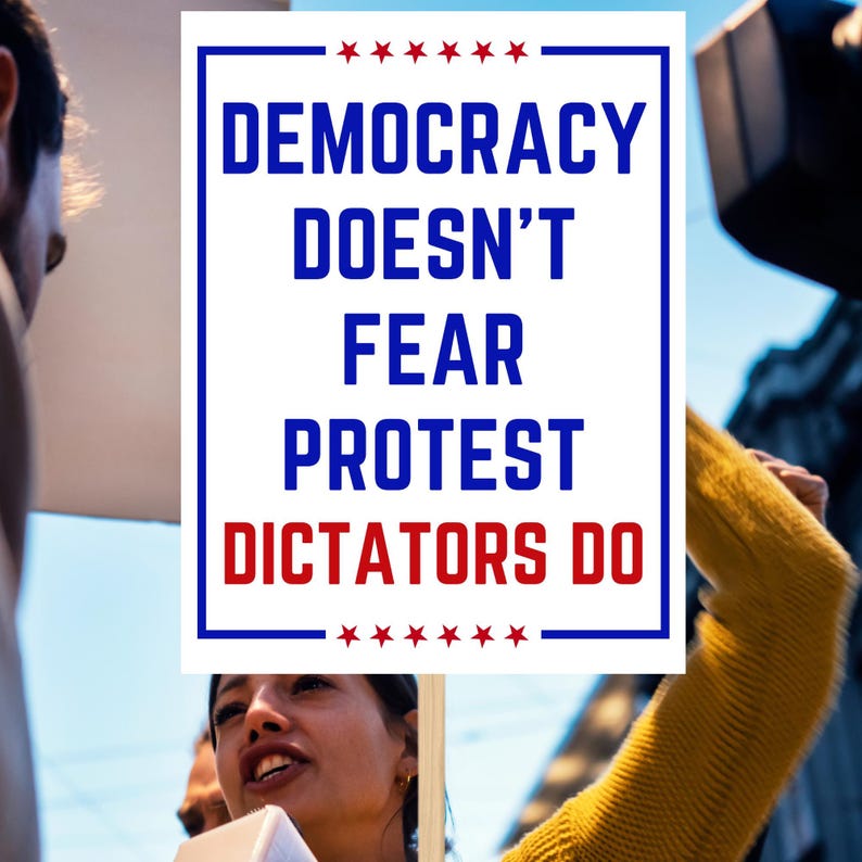 May include: A sign with the text "DEMOCRACY DOESN'T FEAR PROTEST DICTATORS DO" in blue and red, framed by a white border and stars. The image shows a protest with people holding signs.