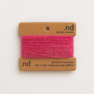 May include: A bright pink yarn spool with the text ".nd Second Cashmere." The yarn is wrapped around a cardboard tag with the text "Reclaimed Cashmere 10m // 2-ply // Approximately 2/28nm."