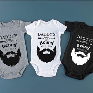 May include: Three baby onesies in gray, white, and black with the text "Daddy's little Beard Puller" and a black and white beard graphic.