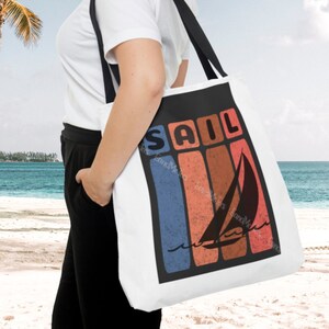 May include: White canvas tote bag with a black handle. The bag has a retro-style graphic of a sailboat with the word "SAIL" in bold letters.