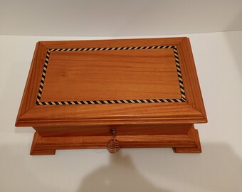 May include: A wooden box with a black and yellow inlay design around the lid. The box has a small, decorative knob on the front.