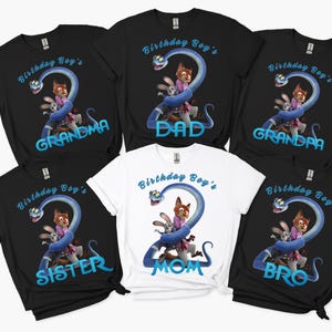 May include: A collection of five black t-shirts and one white t-shirt featuring a graphic of a blue snake forming the number two around a rabbit and a fox. The text reads Birthday Boy's followed by Grandma, Dad, Grandpa, Sister, Mom, or Bro.