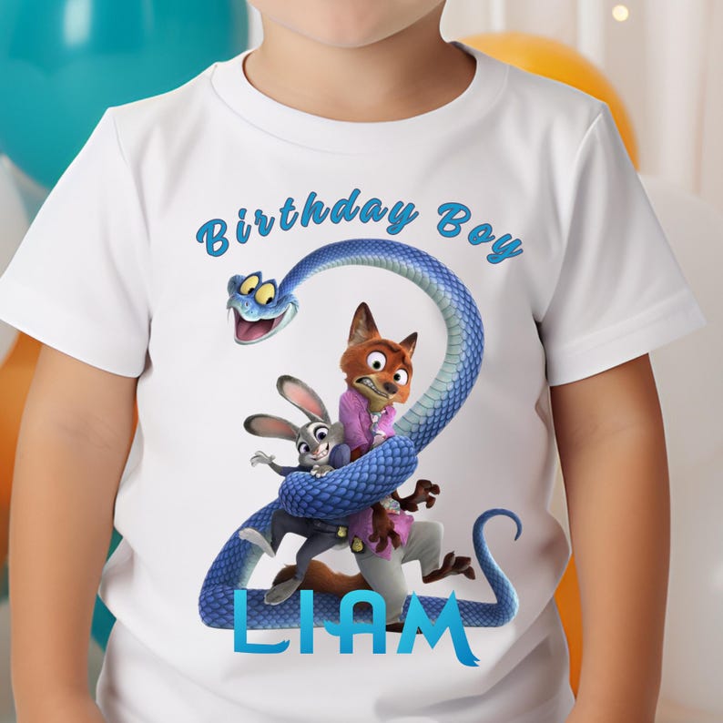 May include: A white short-sleeved t-shirt featuring a graphic of a blue snake coiled into the shape of the number two, with a cartoon fox and rabbit character inside the coils. The text Birthday Boy is printed above and the name LIAM is below.