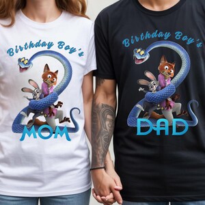 May include: A white t-shirt and a black t-shirt featuring a graphic of a blue snake shaped like the number two, wrapped around a cartoon fox and rabbit. The text reads Birthday Boy's MOM on the white shirt and Birthday Boy's DAD on the black shirt.