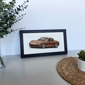 May include: A framed horizontal print featuring a detailed illustration of a metallic copper-colored convertible sports car. The artwork is encased in a simple black rectangular frame with a white mat border, showcasing the vehicle's sleek profile.