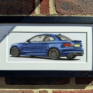 May include: A framed illustration of a blue coupe car shown from a rear three-quarter angle. The vehicle features dark multi-spoke wheels, a rear spoiler, and a yellow license plate. The artwork is enclosed in a simple black rectangular frame.