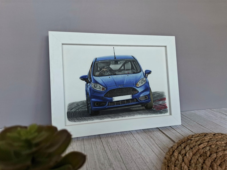 May include: A framed drawing of a blue hatchback car shown from a front-facing perspective. The vehicle features a black honeycomb grille, clear headlights, and a white license plate area, depicted as if driving on a curved track surface.