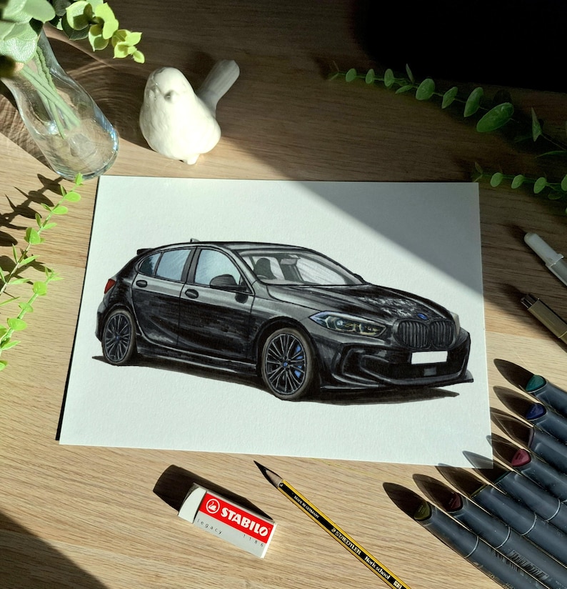 May include: A detailed marker drawing on white paper depicting a black BMW 1 Series hatchback. The vehicle is shown from a front three-quarter angle, featuring dark multi-spoke wheels, a signature kidney grille, and sleek headlights.