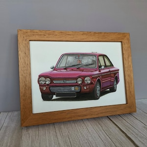 May include: A framed illustration of a vintage maroon two-door sedan. The car features a horizontal front grille, dual round headlights on each side, and a black license plate area. The artwork is encased in a light brown wooden frame.