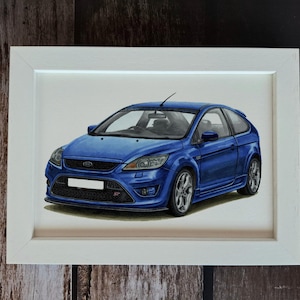 May include: A framed illustration of a blue Ford Focus ST hatchback. The car is depicted in a three-quarter front view, showcasing its signature grille, headlights, and silver alloy wheels. The artwork is enclosed in a simple white frame.