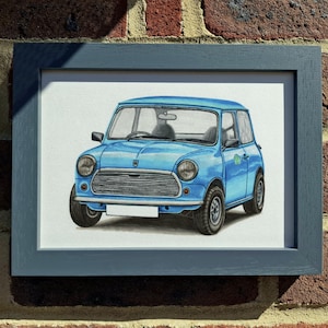 May include: A framed illustration of a light blue compact car featuring a horizontal slatted grille, round headlights, and a blank white license plate. The artwork is encased in a dark gray wooden frame with a clean, rectangular profile.