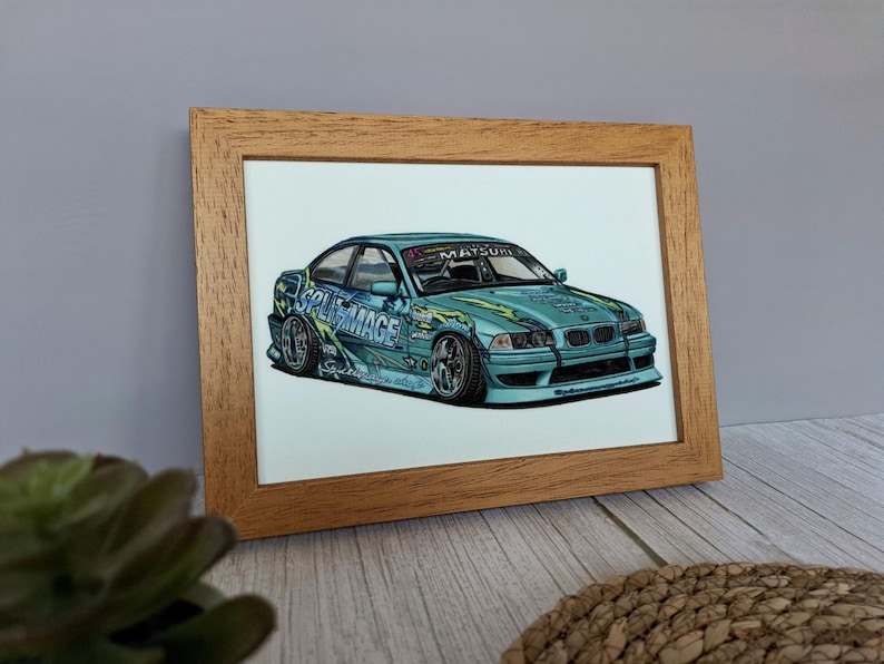 May include: A light blue drift car illustration in a wooden frame. The car features the text SPLIT MAGE and MATSURI on the windshield and body, with green flame-like graphics, low-profile tires, and a lowered suspension in a detailed drawing.