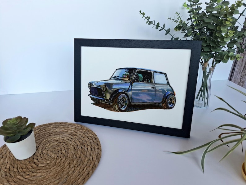May include: A framed art print featuring a detailed illustration of a grey compact car with a boxy silhouette, round headlights, and wide wheel arches. The car is depicted in a side profile view against a plain white background within a black frame.