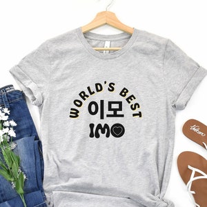 May include: Gray t-shirt with the text "WORLD'S BEST 이모 IMO" in black and yellow lettering with a small heart.