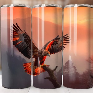 May include: A set of three stainless steel tumblers with a wraparound design featuring a majestic hawk in flight against a sunset backdrop. The hawk's wings are spread, showcasing its brown and red feathers. The background includes mountains and trees.