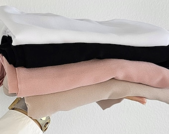 May include: A stack of four folded fabric scarves in white, black, pink, and beige.