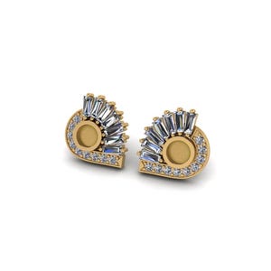 Op de afbeelding: Een paar goudkleurige oorstekers. Elke oorbel heeft een centraal cirkelvormig ontwerp omgeven door kleine, heldere edelstenen. Heldere, rechthoekige edelstenen waaieren uit het midden en creëren een decoratief ontwerp.