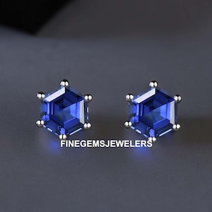 Könnte beinhalten: Ein Paar silberne Ohrstecker mit sechseckigen blauen Edelsteinen. Die Ohrringe sind vor einem grauen Hintergrund platziert.