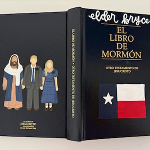 May include: A black book titled "EL LIBRO DE MORMON" with the text "OTRO TESTAMENTO DE JESUCRISTO". The cover features a Texas flag and illustrations of three figures. The spine reads "EL LIBRO DE MORMON OTRO TESTAMENTO DE JESUCRISTO".