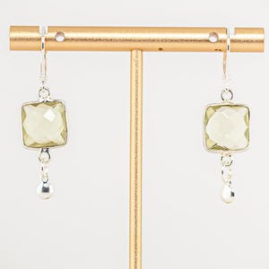 May include: A pair of silver earrings with a light green square gemstone and a small silver ball dangling from each earring.