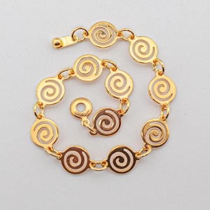 May include: A gold-toned bracelet composed of a series of circular links, each featuring an openwork spiral design. The bracelet is connected by small metal jump rings and includes a circular clasp mechanism with a ball-tipped end piece.