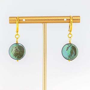 May include: A pair of gold hoop earrings with a large, round, dark green pearl pendant hanging from each hoop.