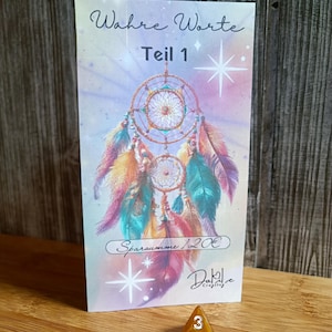 Könnte beinhalten: Eine Karte mit einem Traumfänger-Design, mit dem Text "Wahre Worte Teil 1" und "Sparsumme 120€". Ein goldfarbener dreieckiger Würfel mit weißen Zahlen befindet sich im Vordergrund. Der Hintergrund ist eine Holzoberfläche.