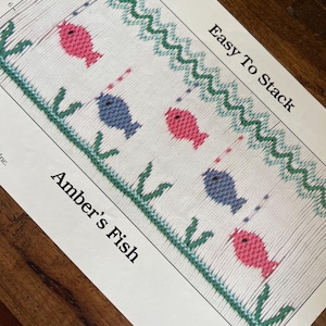 May include: A printed craft pattern titled "Amber's Fish" features a repeating design of pink and blue fish with fishing lines, green seaweed, and a wavy green border. The text "Easy To Stack" is also visible.