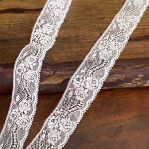 May include: White lace trim with a delicate floral pattern. The lace is approximately 1 inch wide and is perfect for adding a touch of elegance to any project.