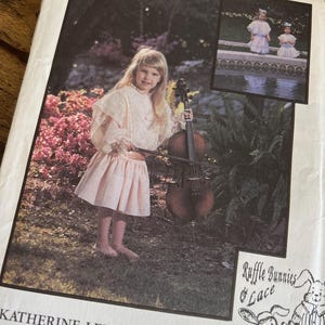 May include: A vintage sewing pattern titled "Ruffle Bunnies & Lace Patterns" featuring a young girl in a pink dress holding a cello. The pattern is by Katherine Lee and is for children's sizes 2-5. The cover includes a smaller image of two girls in similar dresses.