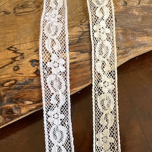 May include: Two pieces of white lace trim with a delicate floral pattern.