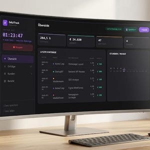 May include: A curved computer monitor displays a dark interface with data visualizations and text. The screen shows time, financial figures, and project details. A keyboard, mouse, and a small plant are on the wooden desk.