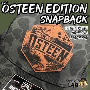 May include: A black and green camouflage trucker hat with a brown leather patch that says "Osteen" and features a deer, alligator, and a sign that says "Lemon Bluff Maytown". The hat also has a black and white logo that says "Lasered Lab" with a golden retriever.