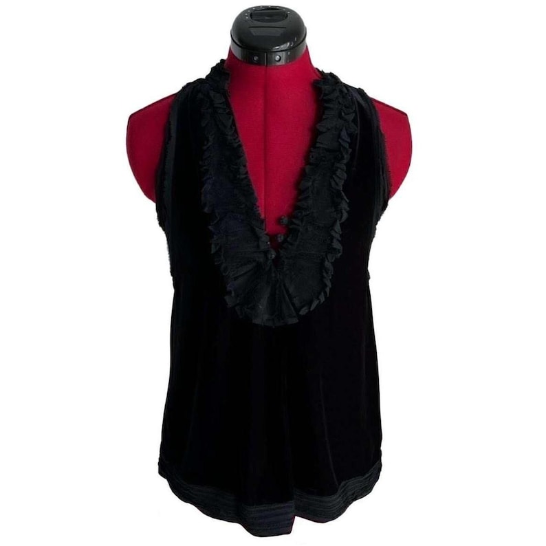 Puede incluir: Top halter de terciopelo negro con cuello con volantes. El top sin mangas tiene un dise&ntilde;o de cuello en V y un ribete decorativo en el dobladillo. El top se muestra en un maniqu&iacute; rojo.