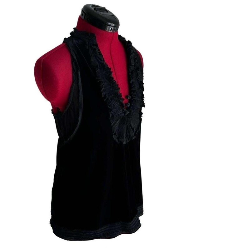 Puede incluir: Top sin mangas de terciopelo negro con cuello y dobladillo con volantes. La parte superior se muestra en un maniqu&iacute; rojo. El escote presenta un detalle de volantes decorativos, que a&ntilde;ade un toque de elegancia a la prenda. El dise&ntilde;o general es simple pero sofisticado.