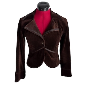 Peut inclure: Un blazer en velours marron foncé doté d'un col à revers cranté avec une bordure décorative sombre, de manches longues et d'une fermeture à un seul bouton sur le devant. La veste présente une coupe ajustée avec un ourlet arrondi.