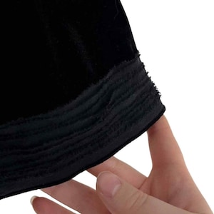 Puede incluir: Primer plano de una tela de terciopelo negro con un borde texturizado y deshilachado. La tela parece suave y lujosa, con un brillo sutil. El detalle del borde a&ntilde;ade un elemento de dise&ntilde;o &uacute;nico a la prenda.