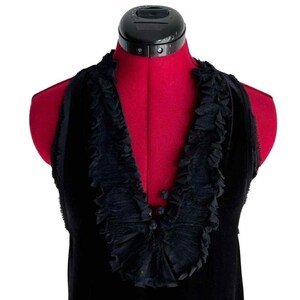 Puede incluir: Un top negro sin mangas con cuello con volantes y tres peque&ntilde;os botones en la parte delantera. El top se muestra en un maniqu&iacute; rojo con un cuello negro ajustable.