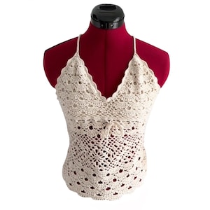 May include: Cream-colored crochet top with a V-neckline and delicate straps. The top features a scalloped edge and a drawstring detail at the waist. The open weave design creates a textured, airy look, perfect for warm weather.