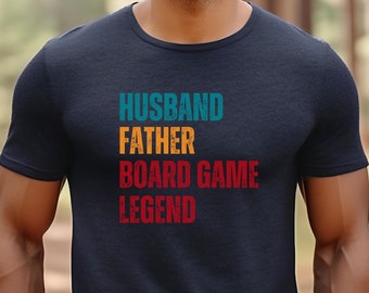 Könnte beinhalten: Ein marineblaues T-Shirt mit dem Text "Husband Father Board Game Legend" in einer Vintage-Schriftart. Der Text ist in verschiedenen Farben, darunter Türkis, Orange und Rot.