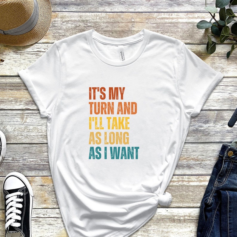 K&ouml;nnte beinhalten: Wei&szlig;es T-Shirt mit einem Vintage-Grafikdruck, der "Es ist mein Zug und ich werde so lange brauchen, wie ich m&ouml;chte." lautet.