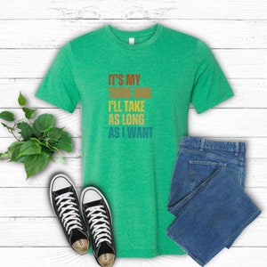 K&ouml;nnte beinhalten: Gr&uuml;nes T-Shirt mit dem Text "It's my turn and I'll take as long as I want" in einer Retro-Regenbogen-Schrift.