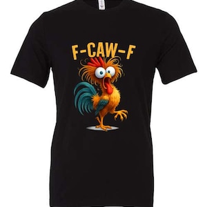 Può includere: T-shirt nera con un disegno di gallo dei cartoni animati. Il gallo ha piume arancioni, gialle e blu e un'espressione sorpresa. Il testo "F-CAW-F" è giallo. Una maglietta grafica divertente.