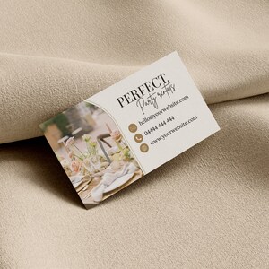 May include: A white business card with brown text that reads "PERFECT Party rentals" with contact information including an email address, phone number, and website address. The background of the card features a blurred image of a table setting with flowers and candles.