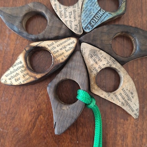 May include: A collection of six wooden thumb page holders, each with a unique design. Some feature newspaper print, while others have a solid wood finish. A green cord is attached to one.