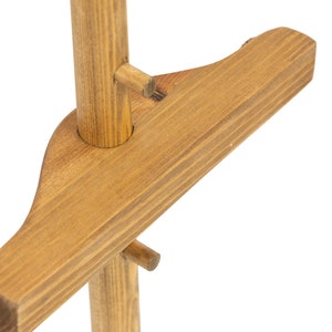 May include: Close-up of a wooden plant stand with a brown stain. The stand has a single post with a horizontal crossbar that is attached to the post with a wooden peg.