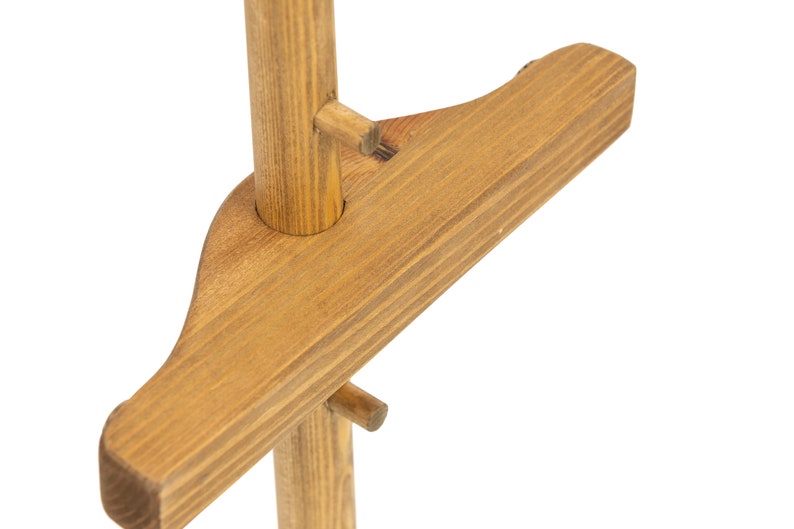 May include: Close-up of a wooden plant stand with a brown stain. The stand has a single post with a horizontal crossbar that is attached to the post with a wooden peg.