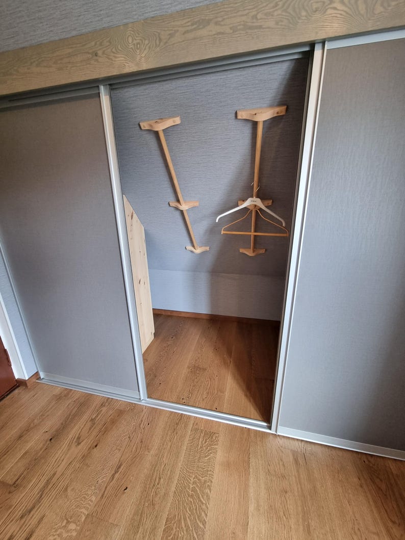 May include: A white closet with sliding doors, a wooden floor, and two wooden hangers hanging from the ceiling.