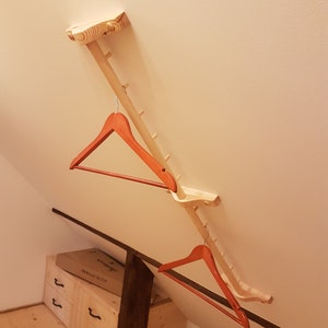 May include: A wooden coat rack with two red hangers attached. The rack is mounted to the ceiling and has a series of small pegs for hanging items.