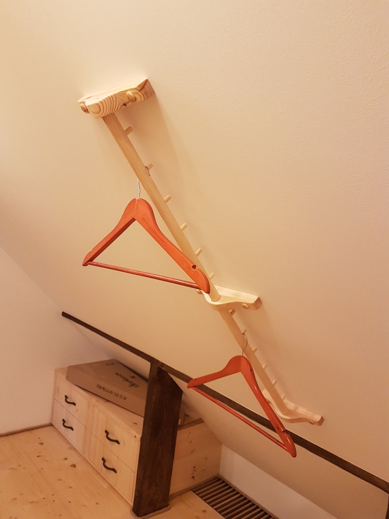 May include: A wooden coat rack with two red hangers attached. The rack is mounted to the ceiling and has a series of small pegs for hanging items.